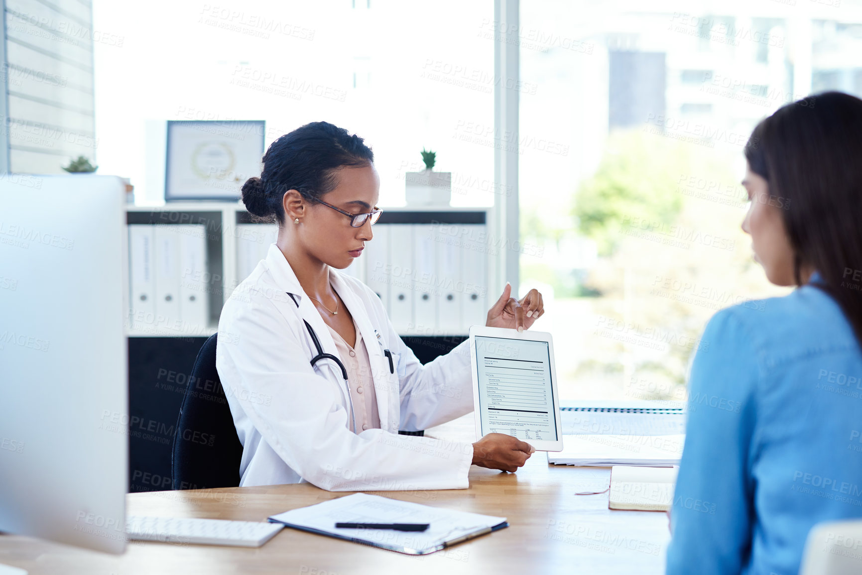 Buy stock photo Shot of a young doctor using a digital tablet during a consultation with her patient