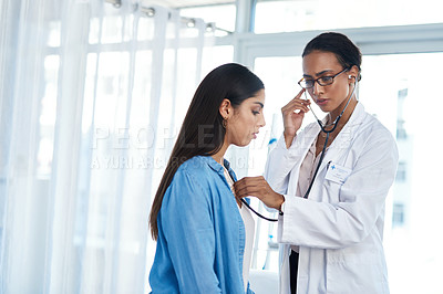 Buy stock photo Shot of a young doctor examining her patient with a stethoscope