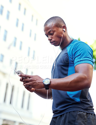 Buy stock photo Shot of a handsome young man listening to music and using his cellphone while exercising outdoors in the city