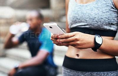 Buy stock photo Shot of an unrecognizable woman using her cellphone while exercising outdoors with her boyfriend resting in the background