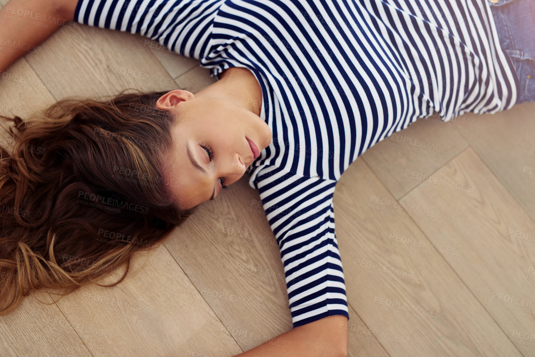 Buy stock photo Cropped shot of an attractive young woman lying down on the wooden floor in her living room during the day