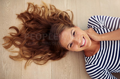 Buy stock photo Cropped portrait of an attractive young woman lying down on the wooden floor in her living room during the day
