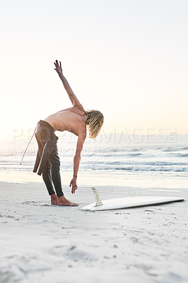 Buy stock photo Full length shot of a handsome young man stretching before going surfing at the beach