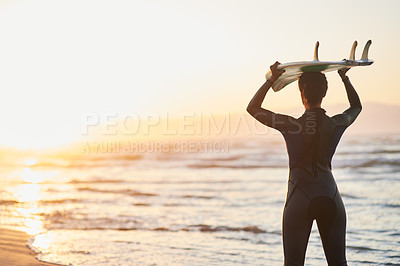 Buy stock photo Rearview shot of a female surfer carrying her surfboard over her head at the beach