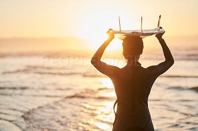 Buy stock photo Rearview shot of a female surfer carrying her surfboard over her head at the beach