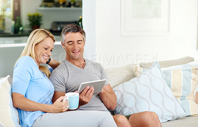 Buy stock photo Cropped shot of a mature couple using a digital tablet while sitting on their sofa at home