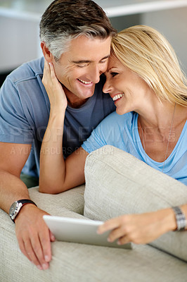Buy stock photo Cropped shot of an affectionate mature couple using a digital tablet while sitting on their sofa at home