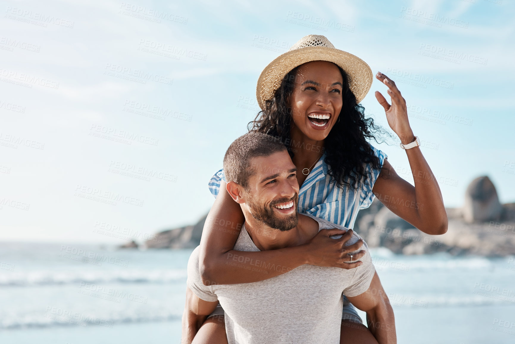 Buy stock photo Shot of a young man piggybacking his girlfriend at the beach