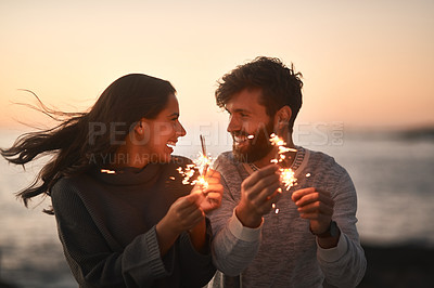 Buy stock photo Love, beach and couple with sparklers for celebration, party and quality time on romantic date. Nature, sunset and happy man and woman with fireworks for honeymoon on holiday, weekend and vacation
