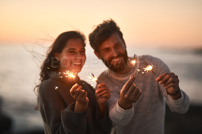 Buy stock photo Happy, beach and couple with sparklers for celebration and party with sparks on romantic date. Love, sunset and excited man and woman with fireworks for honeymoon on holiday, weekend and vacation