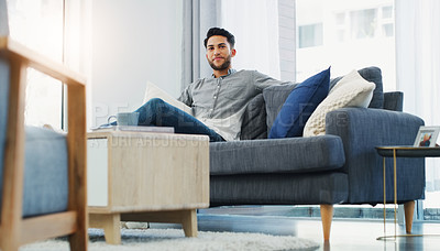 Buy stock photo Cropped shot of a handsome young man sitting on the sofa and relaxing while in the lounge during the day