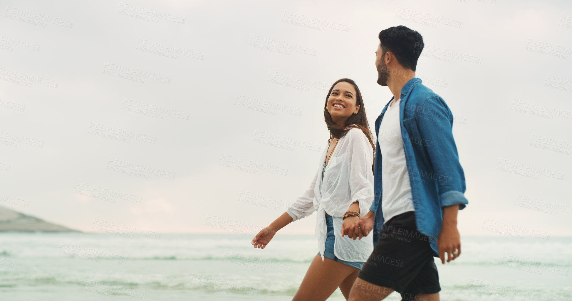 Buy stock photo Cropped shot of an affectionate young couple holding hands and walking along the beach during the day