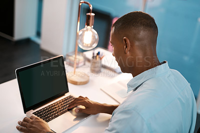 Buy stock photo High angle shot of a young businessman working on his laptop during a late night shift at work