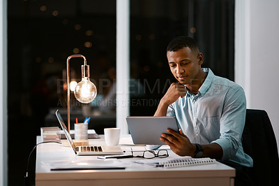 Buy stock photo Shot of a handsome young businessman using a digital tablet while working late in his office