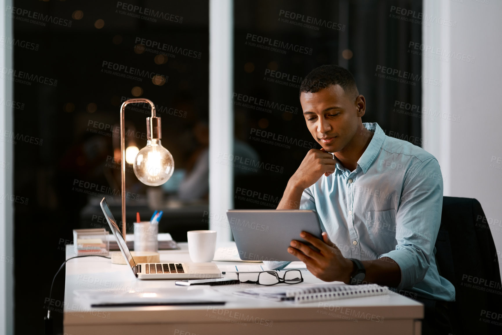 Buy stock photo Shot of a handsome young businessman using a digital tablet while working late in his office