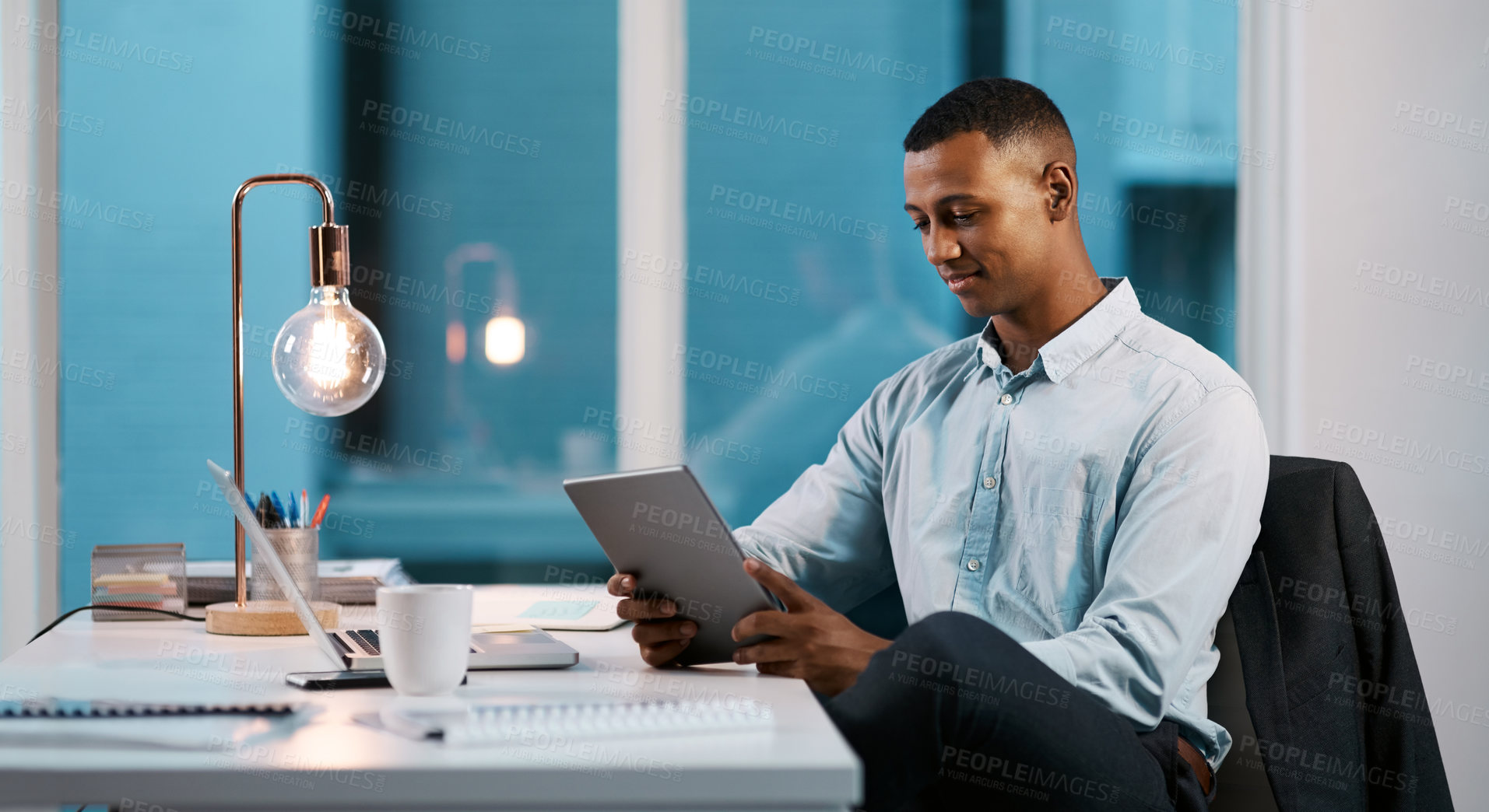 Buy stock photo Shot of a handsome young businessman using a digital tablet while working late in his office