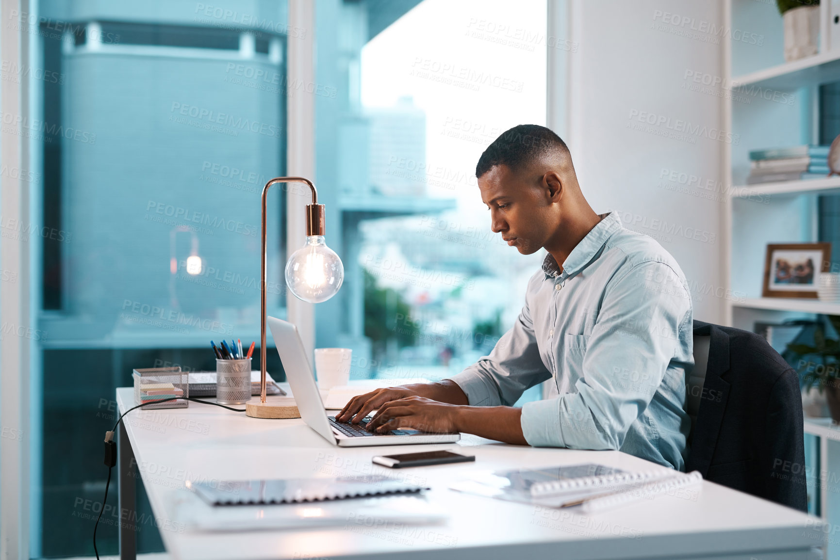 Buy stock photo Shot of a handsome young businessman working on his laptop during a late night shift at work