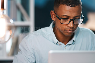 Buy stock photo Shot of a handsome young businessman working on his laptop during a late night shift at work