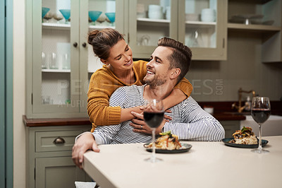 Buy stock photo Shot of an affectionate young woman embracing her husband during supper in their kitchen at home