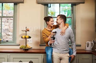 Buy stock photo Cropped shot of an affectionate young couple smiling at each other while holding wine glasses in their kitchen at home