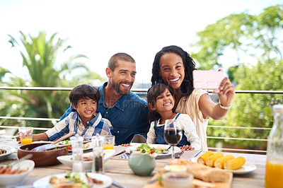 Buy stock photo Shot of a beautiful young family taking pictures with a cellphone while enjoying a meal together outdoors