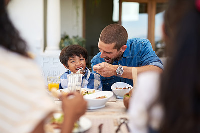 Buy stock photo Shot of a father feeding his young son during a meal with family outdoors