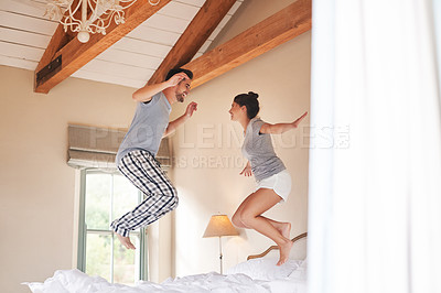 Buy stock photo Full length shot of a cheerful young couple playing and jumping on their bed in their bedroom at home