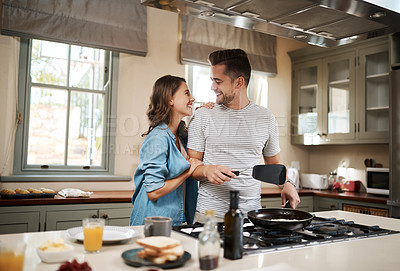 Buy stock photo Shot of a young woman embracing her partner while he cooks breakfast