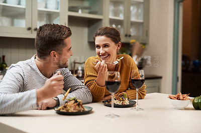 Buy stock photo Shot of an affectionate young couple smiling at each other while enjoying dinner in their kitchen at home