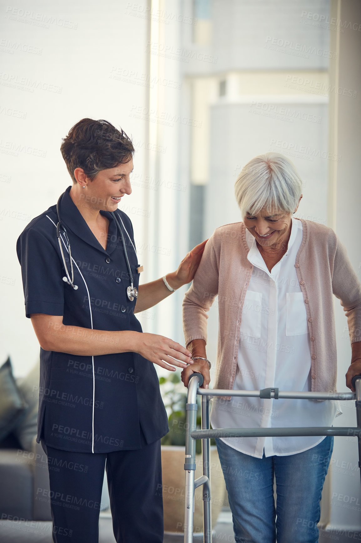 Buy stock photo Cropped shot of a young female nurse assisting a senior woman walk using a walker in a nursing home