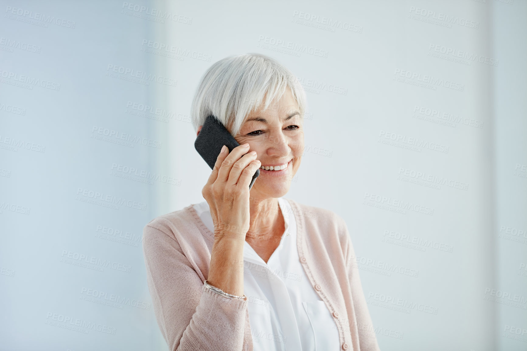 Buy stock photo Cropped shot of a happy senior woman taking a phonecall while standing indoors in a retirement home