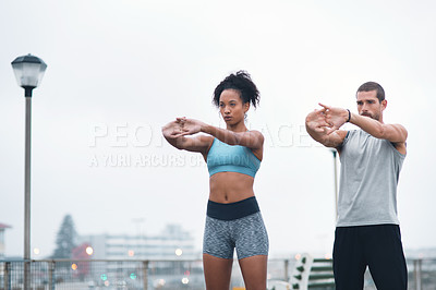 Buy stock photo Shot of two sporty young people stretching while exercising outdoors
