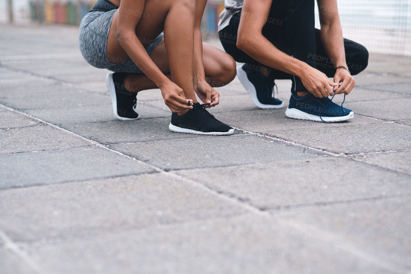 Buy stock photo Closeup shot of two unrecognisable people tying their laces while exercising outdoors