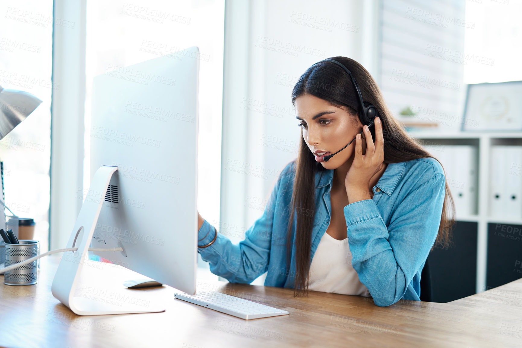 Buy stock photo Shot of a young businesswoman wearing a headset while working on a computer in an office