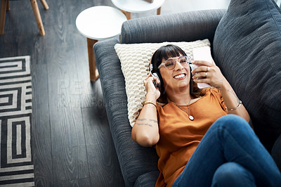 Buy stock photo Shot of a young woman wearing headphones while relaxing at home