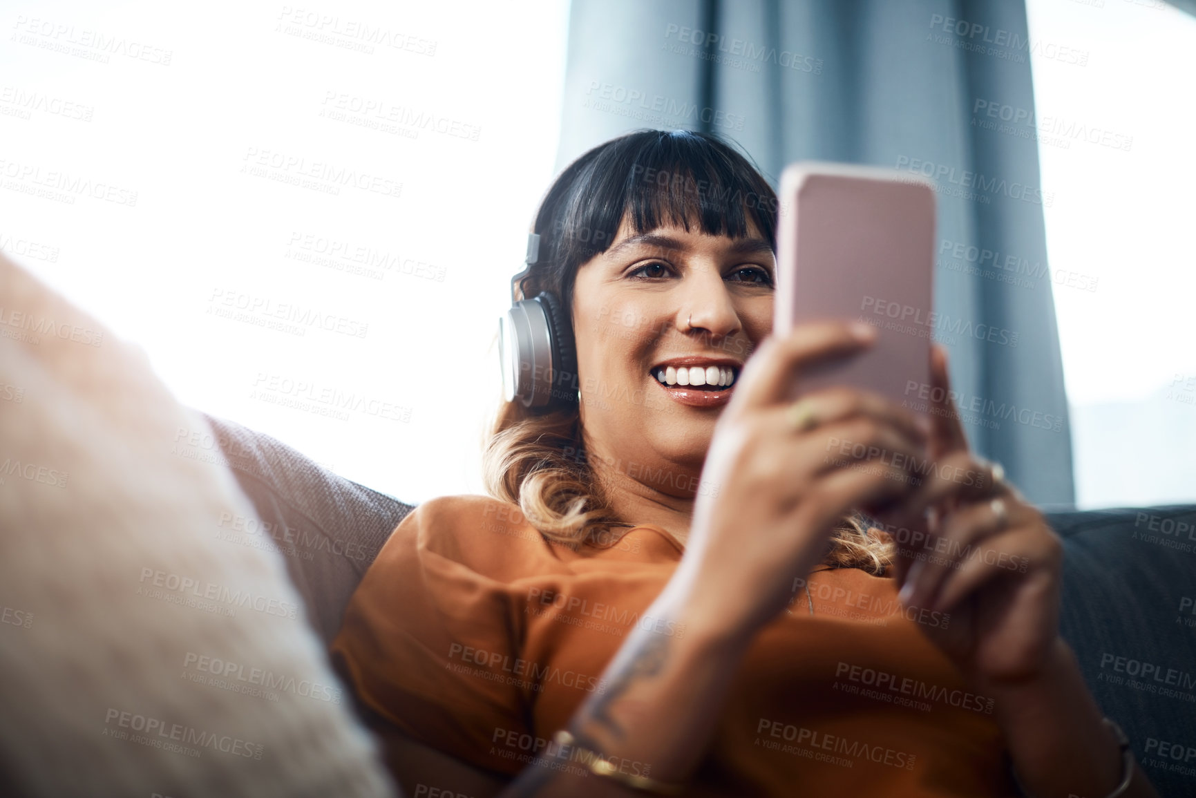 Buy stock photo Girl, home and laughing on smartphone with headphones on couch for streaming funny videos on website. Female person, living room and happy with online subscription for podcast and comedy for fun