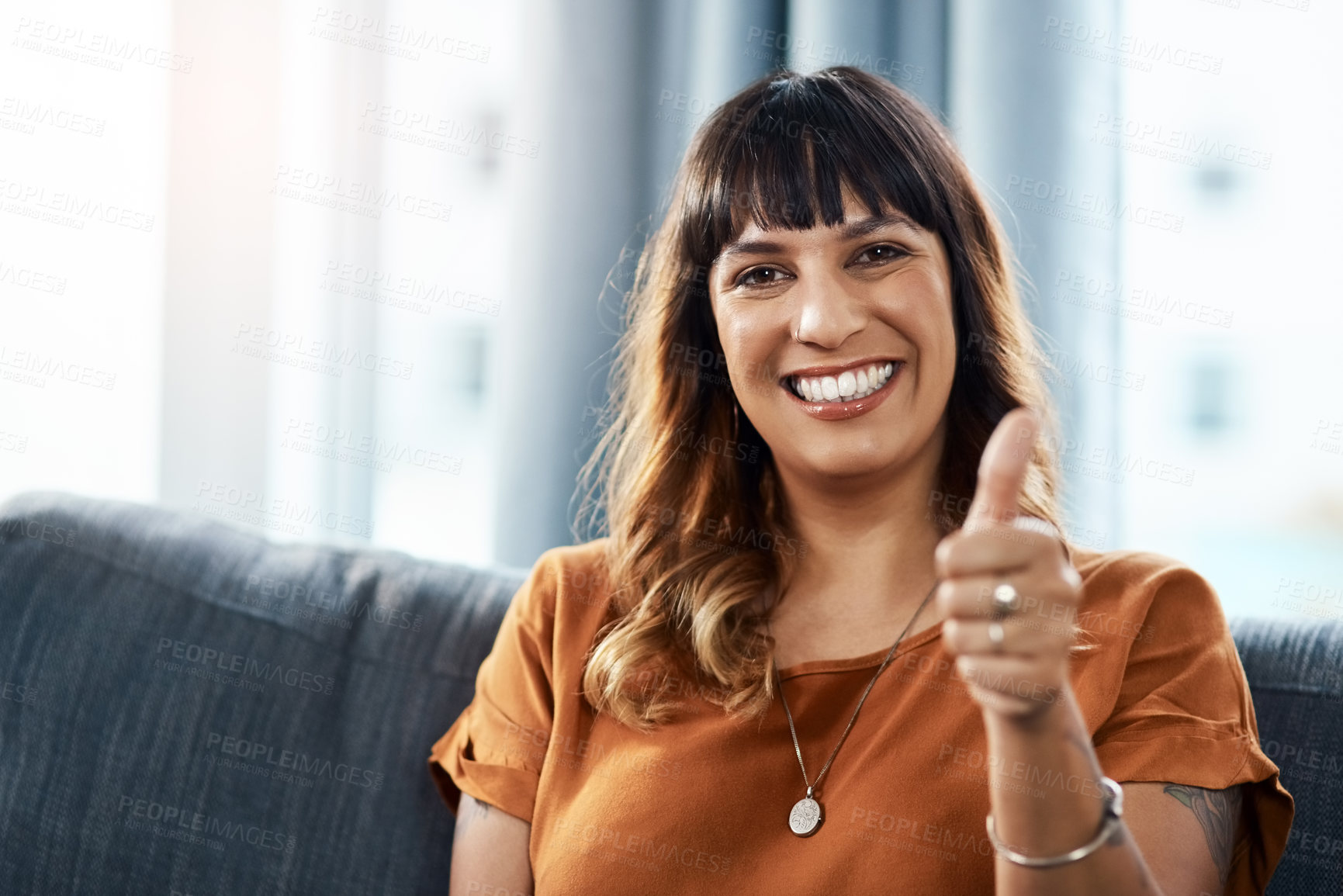 Buy stock photo Shot of a young woman showing thumbs up while relaxing at home