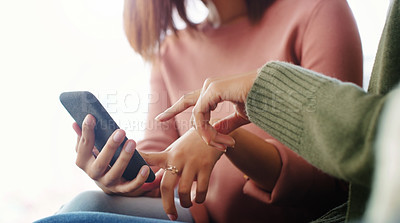 Buy stock photo Cropped shot of two unrecognizable women using a cellphone while sitting on the sofa in a living room