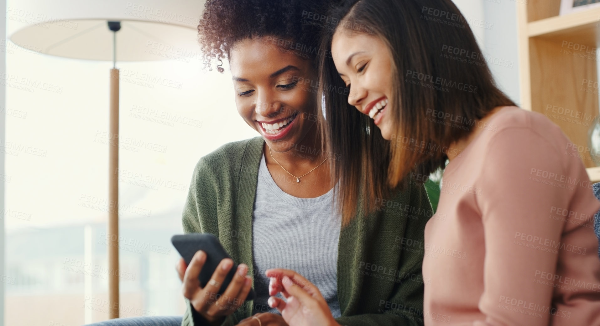 Buy stock photo Cropped shot of two attractive young women using a cellphone while sitting on the sofa in a living room