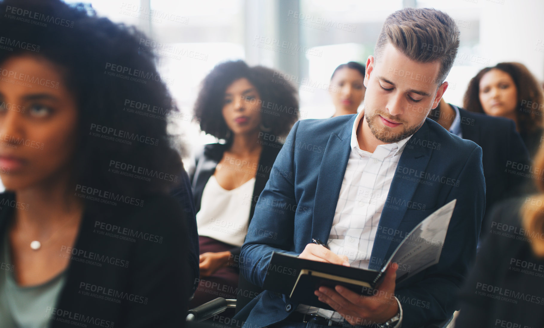 Buy stock photo Shot of a young businessman taking down notes while sitting in the audience of a business conference