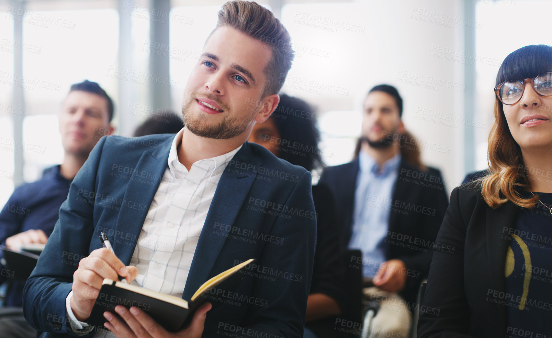 Buy stock photo Shot of a young businessman taking down notes while sitting in the audience of a business conference