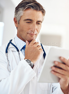 Buy stock photo Cropped shot of a handsome mature male doctor holding a digital tablet while standing in a hospital corridor