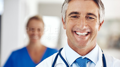 Buy stock photo Portrait of a handsome mature male doctor standing in the hospital with a female colleague in a the background