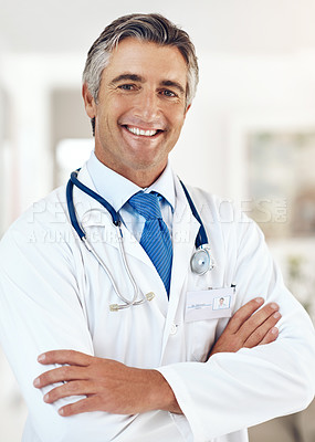 Buy stock photo Cropped portrait of a handsome mature male doctor standing with his arms crossed in the hospital
