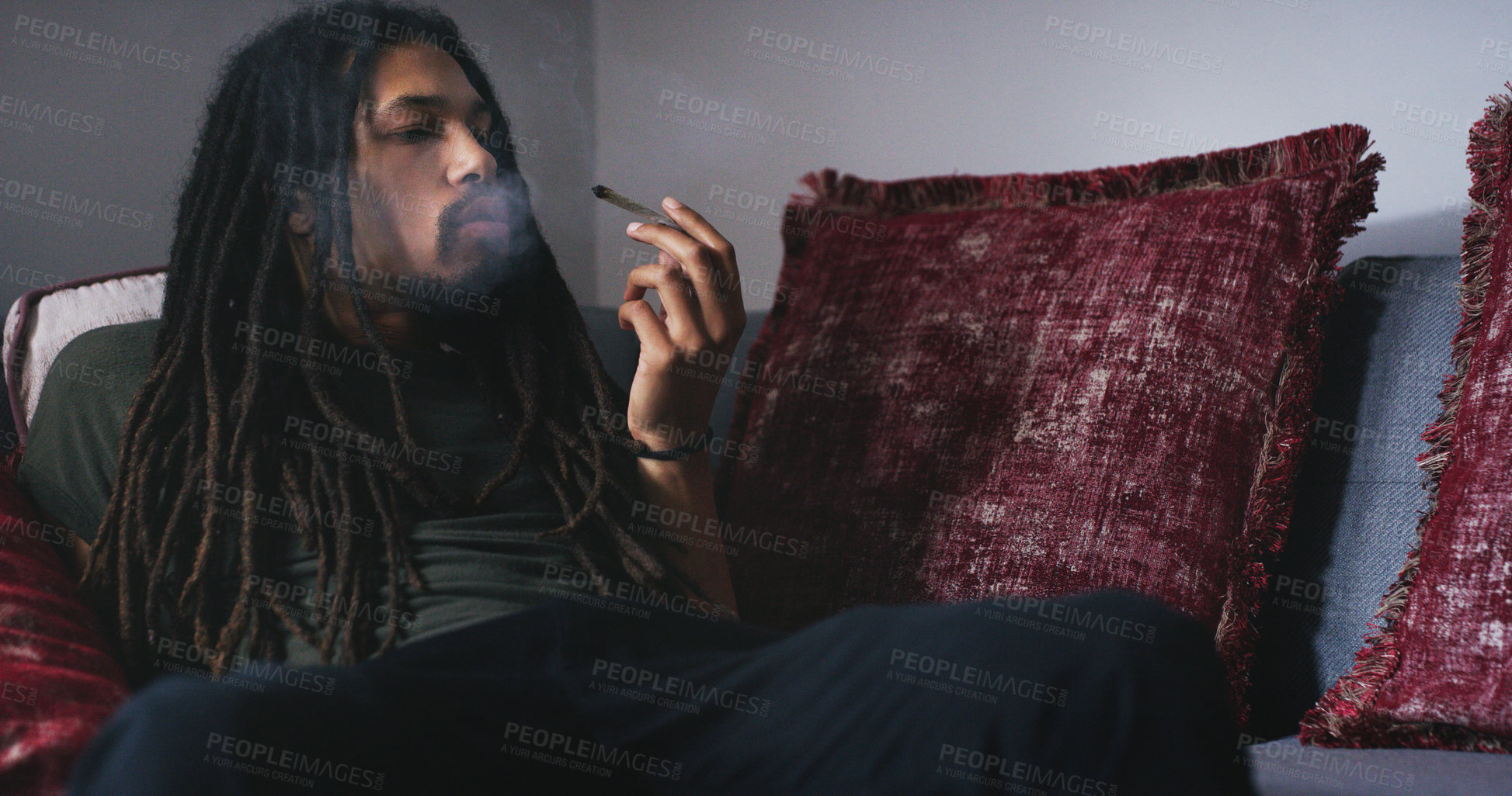 Buy stock photo Shot of a young man smoking a marijuana joint at home