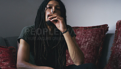 Buy stock photo Shot of a young man smoking a marijuana joint at home