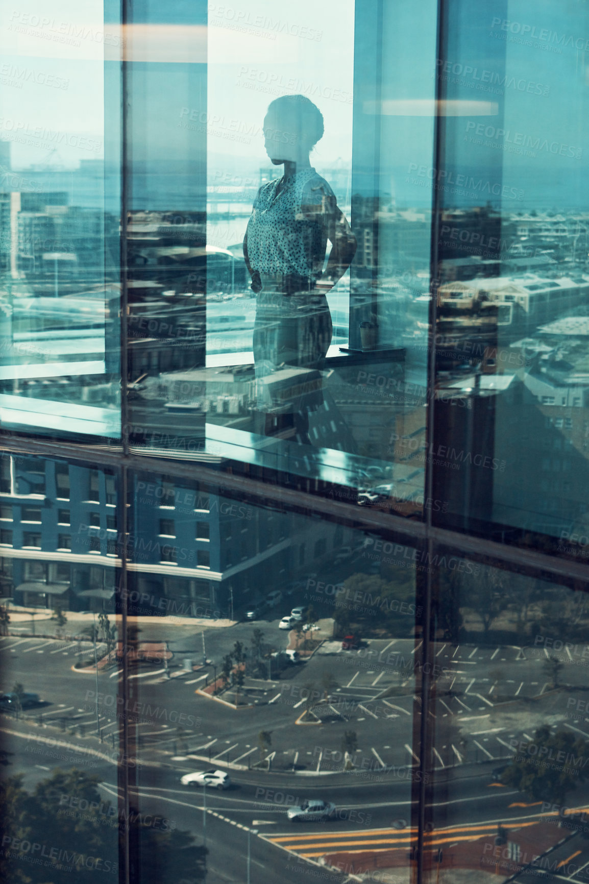 Buy stock photo Shot of a businesswoman standing inside a glass building with a reflection of the city in the background