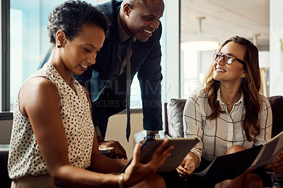 Buy stock photo Shot of a group of businesspeople using a digital tablet while going over some paperwork in their office
