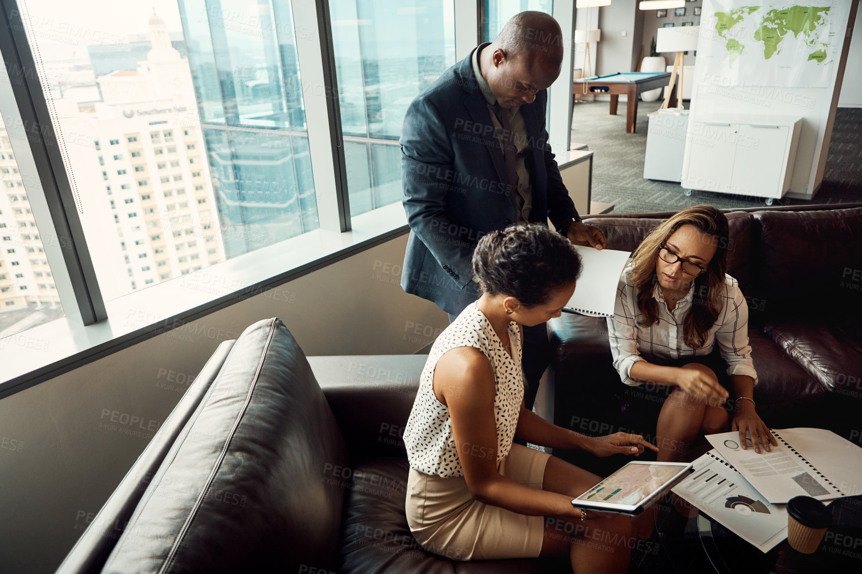 Buy stock photo High angle shot of a group of businesspeople using a digital tablet while going over some paperwork in their office