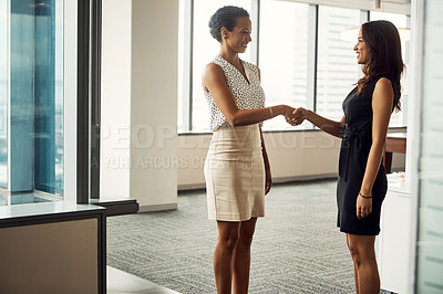 Buy stock photo Shot of two attractive young businesswomen shaking hands in an office